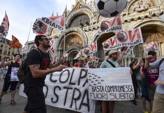 People hold flags and banners as they arrive in San Marco square in Venice at the end of a demonstration called by the No Great Ships movement against big cruise ships sailing into the Venice lagoon on June 8, 2019.