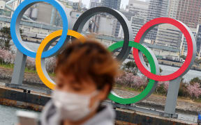 A woman wearing a mask walks near the Olympics' mark in Odaiba, Tokyo on February 22, 2020, amid the outbreak of a new coronavirus in Japan.