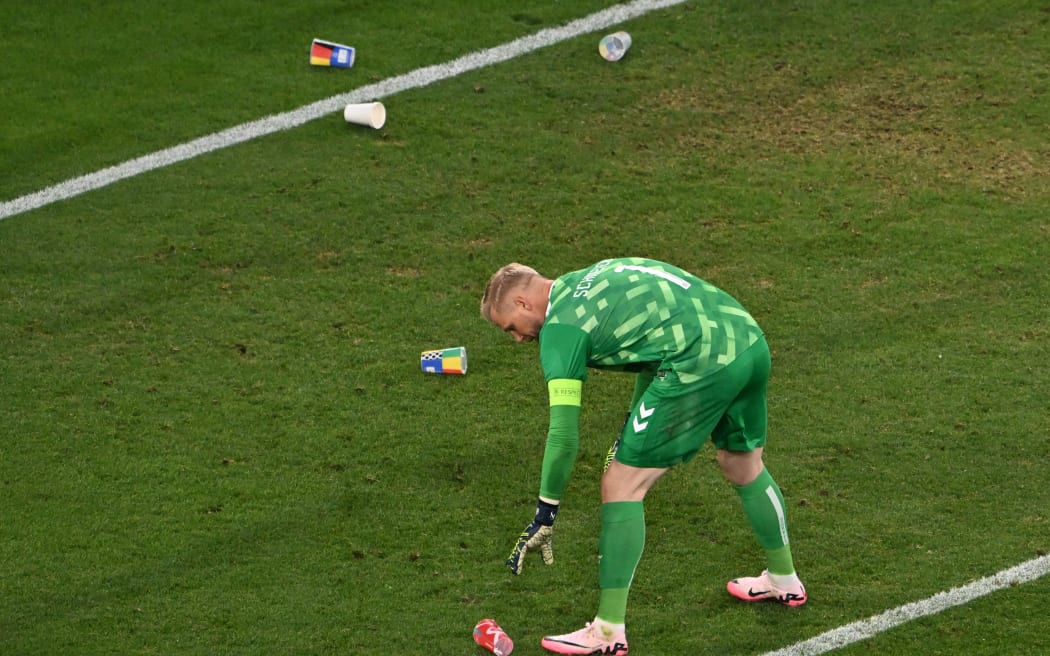 Denmark's goalkeeper Kasper Schmeichel collects beer cups lying on the pitch during Euro 2024.