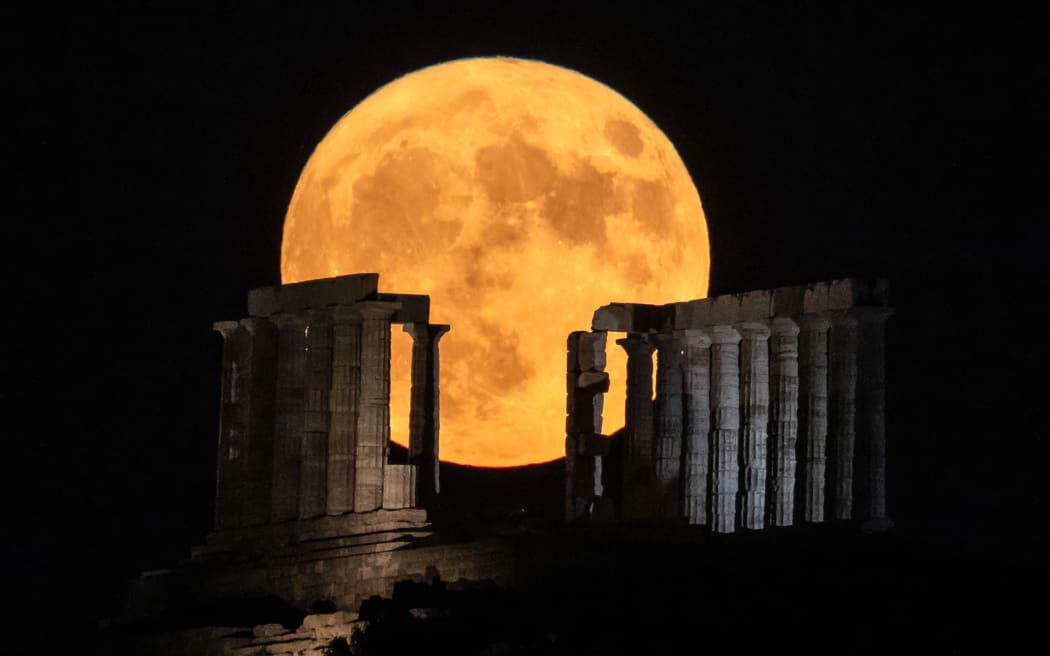 The full moon rises behind the ancient temple of Poseidon at cape Sounion, south of Athens on August 1, 2023. (Photo by Aris MESSINIS / AFP)