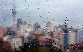 Urban view of rain drops falls on a window during a stormy day overlooking Auckland CBD New Zealand skyline in the background.