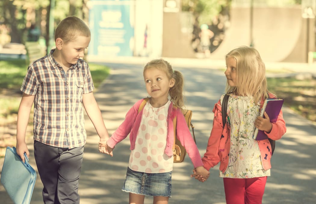 A photo of little pupils walking from school after lessons by holding hands
