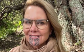 Dr Hinemoa Elder, wearing a brown scarf and brown jacket, holds a copy of her new book Ara.