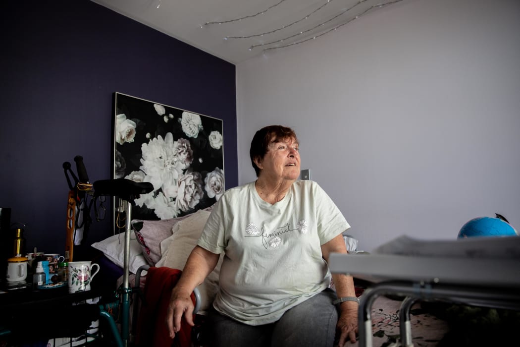 Lorri Mackness sitting on the bed in her apartment looking out to the window.