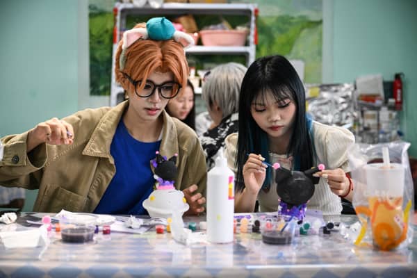This photo taken on August 14, 2024 shows cosplayer Xu Yunting (L), dressed as Jesse, a male character from the video game 'Light and Night', and Feng Xinyu visiting a crafts shop during their 'cos commissioning' date in Shanghai.