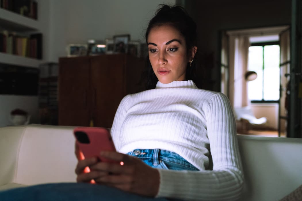 Young woman looking at her phone at home (Photo by Eugenio Marongiu / Cultura Creative / Connect Images via AFP)