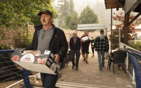 Community members bring supplies down to boats to move across Shuswap Lake for high alert and evacuated community areas without road access, as the Bush Creek East fire continues to burn in Blind Bay, British Columbia, August 21, 2023. Around 30,000 people were under orders from August 19 to evacuate their homes in western Canada's British Columbia, provincial officials said, as a raging wildfire bore down on the city of Kelowna. (Photo by Paige Taylor White / AFP)