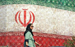 A woman walks past a billboard displaying Iran’s national flag at Enghelab Square in Tehran on 14 June 2026.