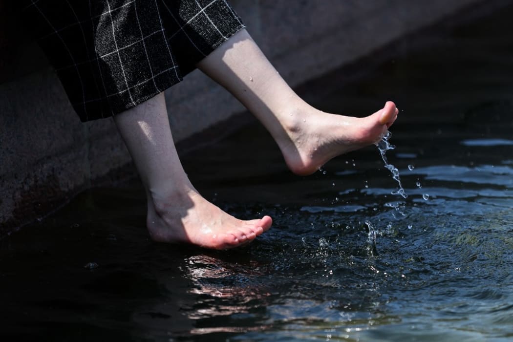 A young woman cools off her feet in a fountain  on a hot spring day, in Moscow,