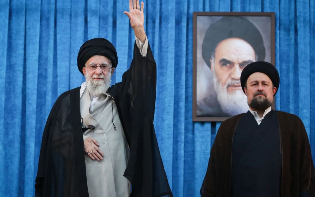 A handout picture provided by the Iranian supreme leader Ayatollah Ali Khamenei's office shows him waving as he stands next to Hassan Khomeini (R), grandson of the founder of Islamic Republic, Ayatollah Ruhollah Khomeini, during a ceremony on the occasion of 36rd death anniversary of the latter, in Tehran on June 4, 2025. Khamenei said on June 4 a United States proposal for a nuclear deal was against the country's national interest amid a public standoff over Tehran's uranium enrichment. (Photo by KHAMENEI.IR / AFP) / === RESTRICTED TO EDITORIAL USE - MANDATORY CREDIT "AFP PHOTO / HO / KHAMENEI.IR" - NO MARKETING NO ADVERTISING CAMPAIGNS - DISTRIBUTED AS A SERVICE TO CLIENTS ===