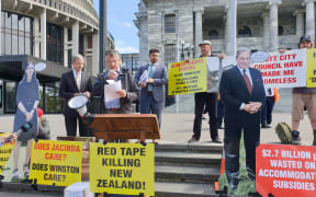 Colin Wightman speaking in a microphone at the grounds of Parliament in protest for legislation to protect tiny houses.