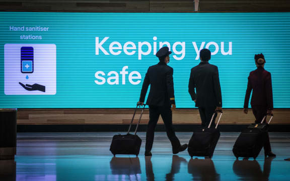 Qatar Airlines flight crew members walking past an illuminated sign displaying a message relating to the Covid-19 novel coronavirus at the Sydney International Airport in Sydney, October 2020.
