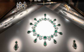 A lavish jewelled necklace lies with some matching earrings on an illuminated surface.