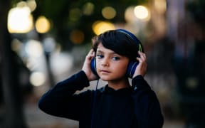A child listening to headphones, with their hands on each headphone, wearing a dark-coloured top.