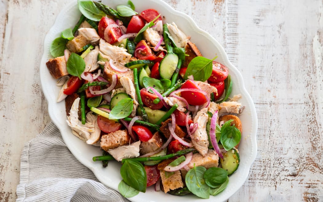 An oval serving dish containing a salad of toasted bread, basil, asparagus, red onion, tomatoes and rotisserie chicken.