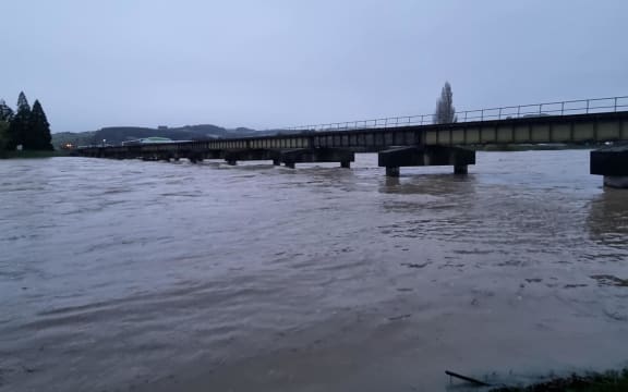 The Mataura River at Gore is flowing swiftly and some debris is caught under a rail bridge.