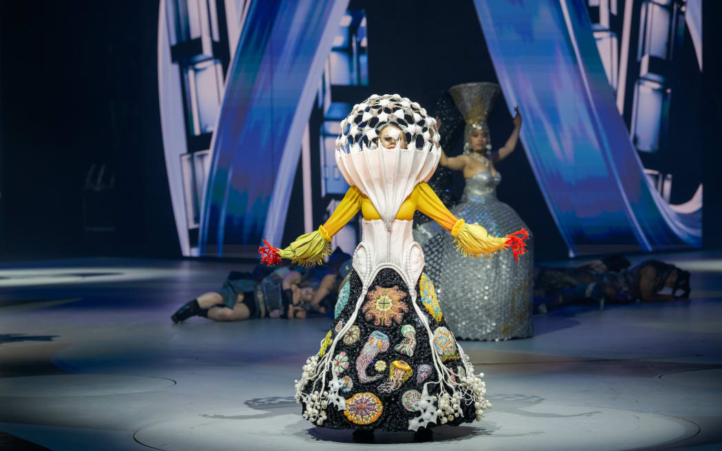 An elaborate costume with a conical headpiece and botanical drawings on the skirt.