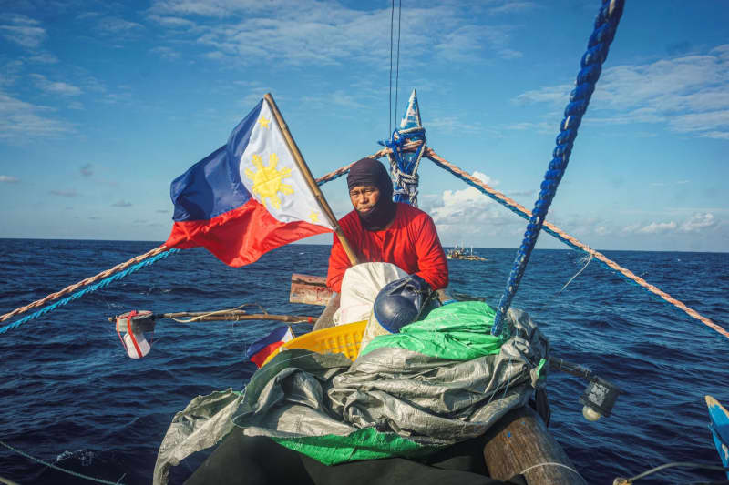 A man on a small boat in the middle of the sea holding the Philippines flag.
