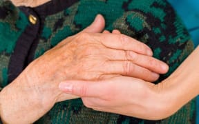 A young doctor holds an elderly woman's hand.