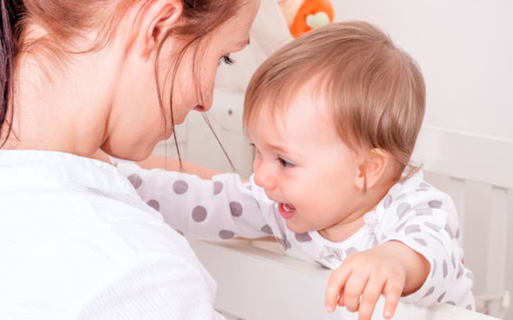A photo of a baby who is having bad dreams with her mother standing at the cot.