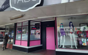 The closed pink door and shop windows on the main street running through Eketāhuna, with Tabu shop sign above