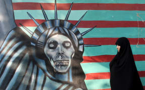 A woman in Tehran walks past a mural on the wall of the former US embassy.