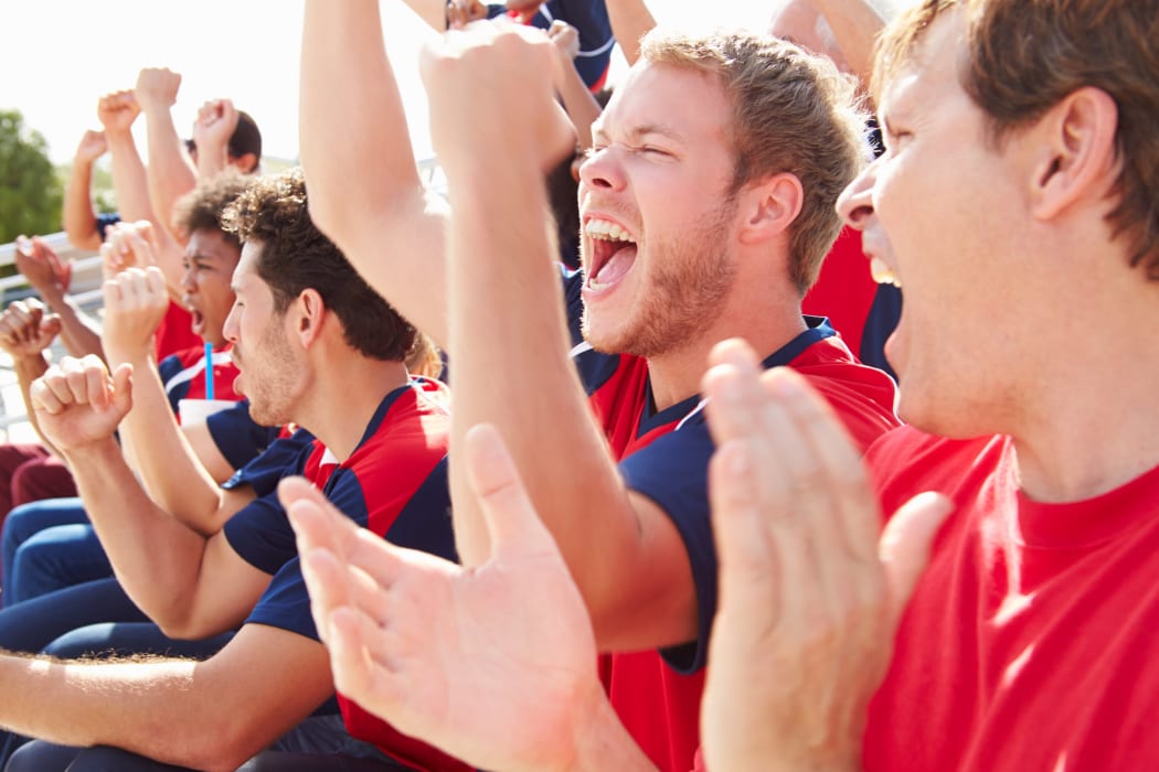 A photo of a line of spectators in red clothing, shouting and clapping in support of their team.