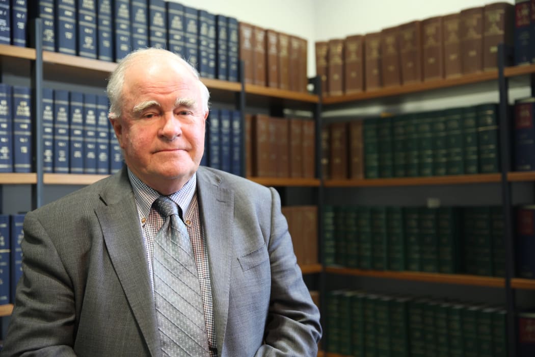 Chief Coroner Judge Neil McLean standing in front of bookshelves, wearing a suit