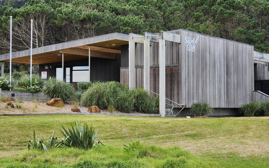 A large, modern-looking building surrounded by grass and forest in the background.