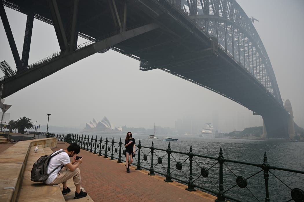 Tourists wearing masks take photos under the Sydney Harbour Bridge enveloped in haze caused by nearby bushfires, in Sydney on December 10, 2019.