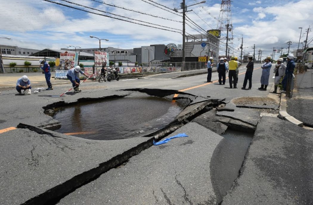 Workers stand by a partially collapsed road following an earthquake in Takatsuki, north of Osaka prefecture on 18 June, 2018.