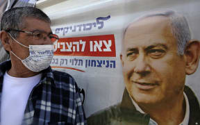 An Israeli man, wearing a mask with the Likud party logo, looks at a poster of Israeli Prime Minister Benjamin Netanyahu, chairperson of the party, in Israel's southern city of Beersheva on March 7, 2021, ahead of the legislative election.