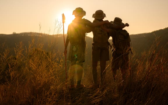 silhouette of male students standing and hugging each other in the grass on the mountain Boy Scouts rejoice at rock climbing success in the evening at sunset.