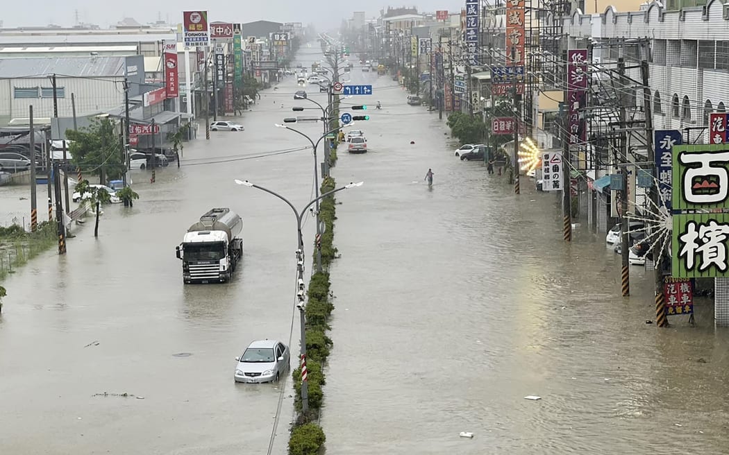 People and vehicles wade through the water along a street that was flooded by Typhoon Gaemi in Kaohsiung on July 25, 2024. The typhoon -- the strongest to hit Taiwan in eight years -- had already forced authorities on the island to close schools and offices, suspend the stock market and evacuate thousands of people.