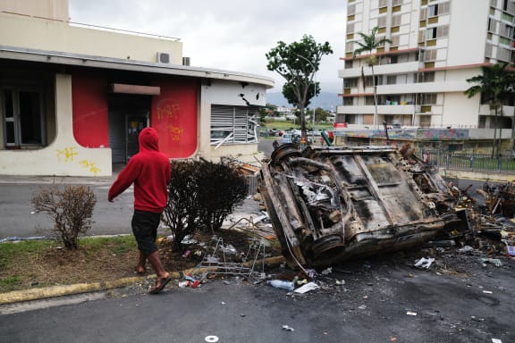 A man walks past a burnt vehicle at an independantist roadblock at Magenta Tour district in Noumea, France's Pacific territory of New Caledonia, on May 22, 2024. The Pacific territory of 270,000 people has been in turmoil since May 13, when violence erupted over French plans to impose new voting rules that would give tens of thousands of non-indigenous residents voting rights. The unrest has left six people dead, including two police, and hundreds injured. (Photo by Theo Rouby / AFP)