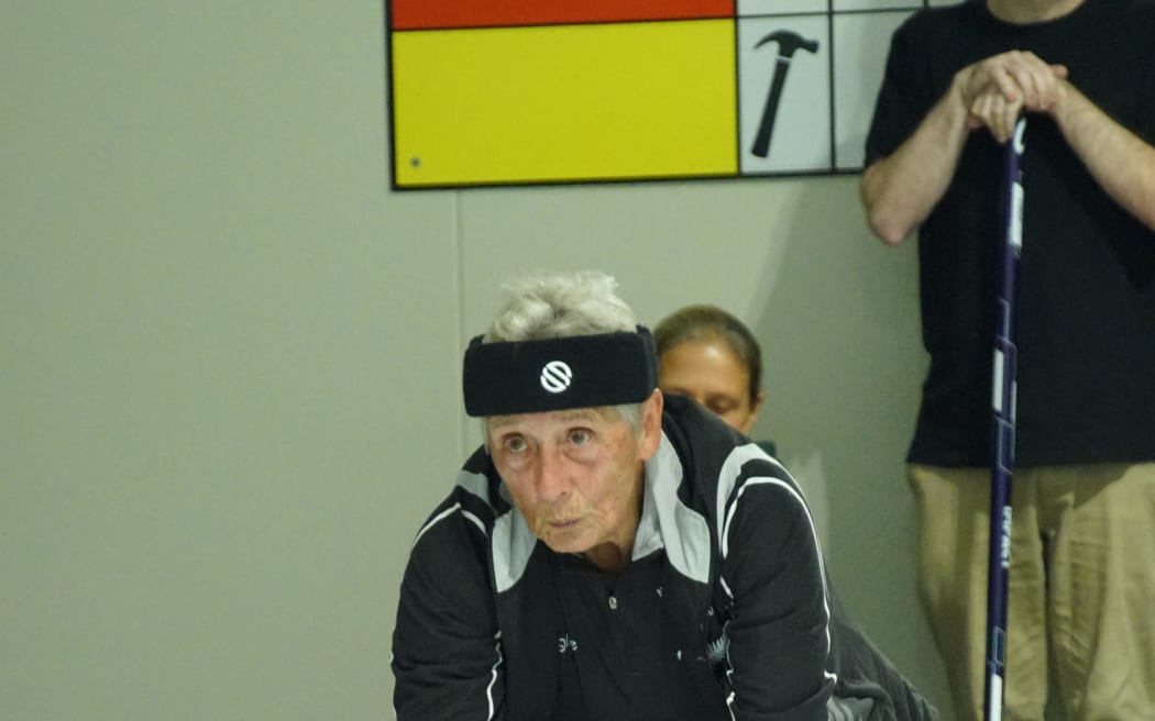 Picture shows an older woman ready to throw a curling stone.