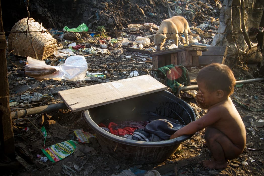 A child washes his face with laundry water among the trash and dogs in Tondo Landfill, Manila