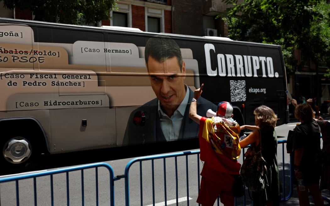 A bus bearing an image of Pedro Sanchez next to a writing reading 'corrupted' drives past supporters of Spain's Prime Minister, in front of Spain’s Socialist party (PSOE) headquarters during a Socialist federal committee in Madrid on July 5, 2025. The minority left-wing coalition government suffered a harsh blow with the jailing of ex-Socialist heavyweight Santos Cerdan for alleged corruption. Sanchez will chair a Socialist federal committee in Madrid on July 5, 2025 that will elect Cerdan's successor, while on July 9 he will appear in parliament to give explanations on the corruption case. (Photo by OSCAR DEL POZO / AFP)