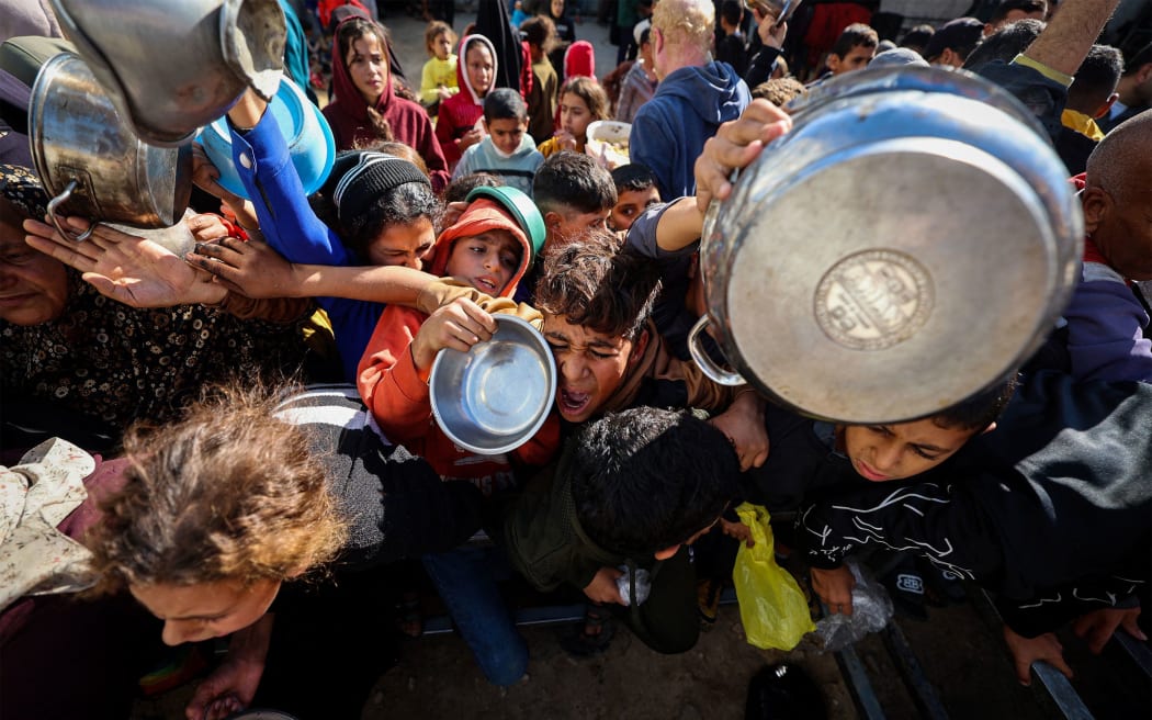 Displaced Palestinians gather to receive food portions at a charity kitchen in the Nuseirat refugee camp in the central Gaza Strip on December 20, 2025.
