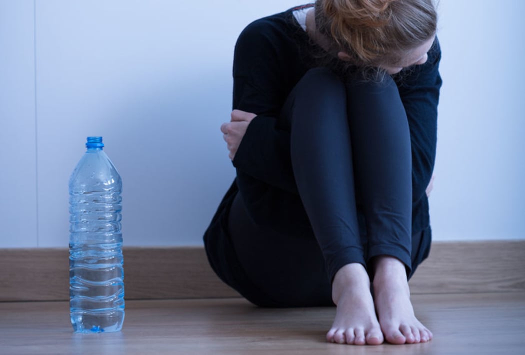 Photo of a sad looking anorexic girl with a bottle of water beside her