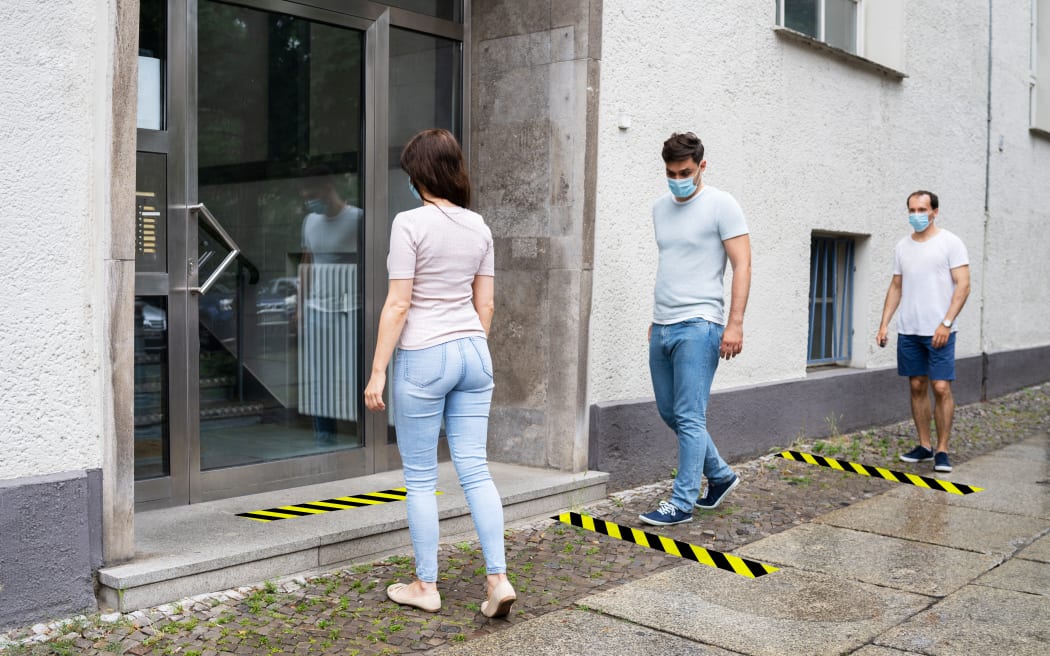 People wearing masks queue while social distancing.