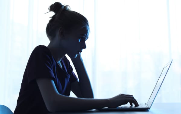 Upset teenage girl with laptop at table indoors. Danger of internet