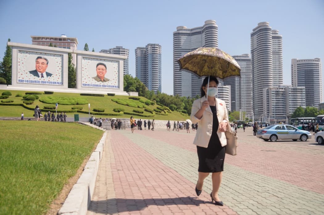A woman holding a parasol walks on Chongjin street before the portraits of late North Korean leaders Kim Il Sung and Kim Jong Il in Pyongyang on May 18, 2021. (Photo by KIM Won Jin / AFP)