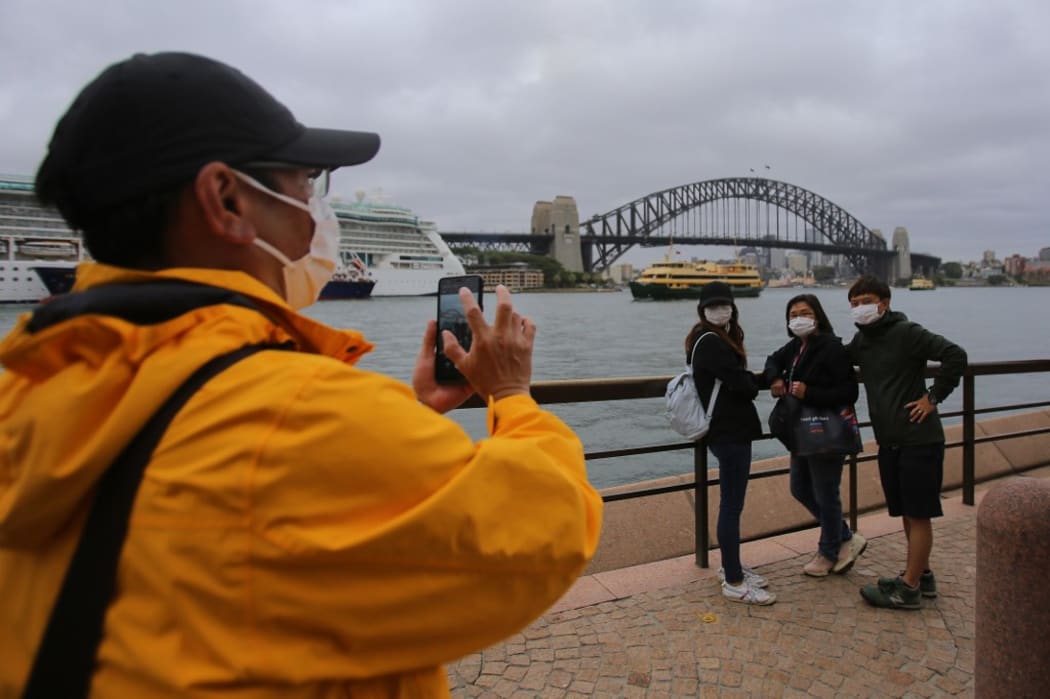 People wear face masks as a preventative measure against Coronavirus COVID-19 in front of the Sydney Harbour Bridge in Sydney, Australia on March 14, 2020.