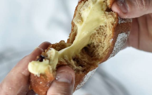 Two hands pull apart a golden doughnut that is oozing pale yellow vanilla custard.