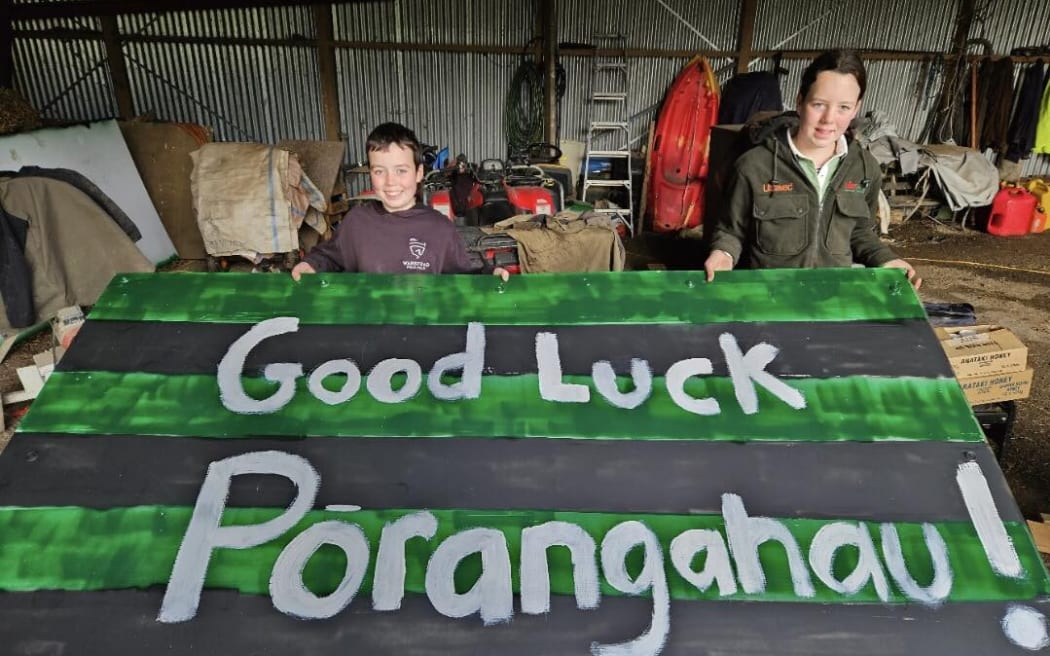 Two children hold a good luck Porangahau sign, painted green and black.