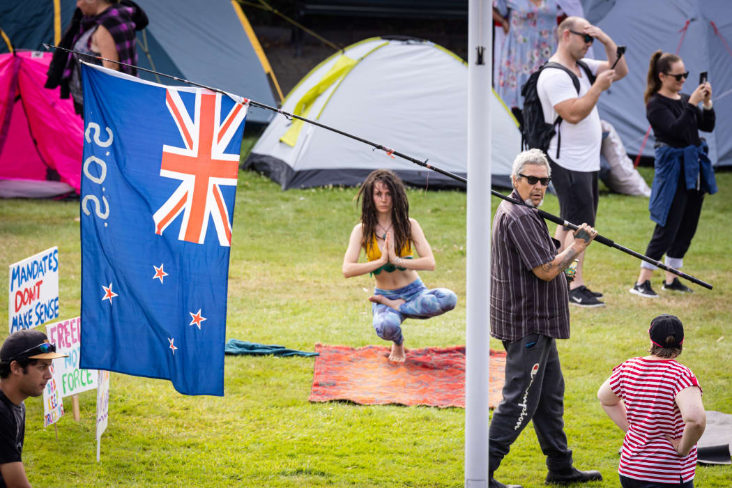 On Parliament's lawn one Covid-19 mandate protestor roams with a flag while another performs yoga