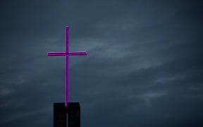 A neon cross lit up against a moody early morning sky