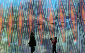 Two silhouetted figures stand in front of a large colourful artwork.