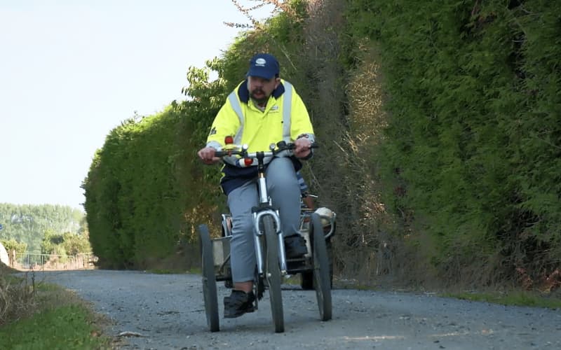 Andy riding a bike on the farm, wearning a bright yellow high viz Fonterra jersey, on his way to meet the milk tanker.